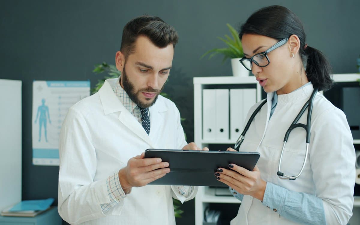 دو پزشک در حال بررسی پروندهٔ بیمار روی تبلت؛ پرونده الکترونیک مطب